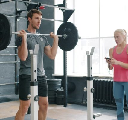 Strong guy is lifting barbell training with weight-lifting indoors in gym working with woman coach. Active lifestyle, motivation and youth concept.
