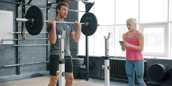 Strong guy is lifting barbell training with weight-lifting indoors in gym working with woman coach. Active lifestyle, motivation and youth concept.