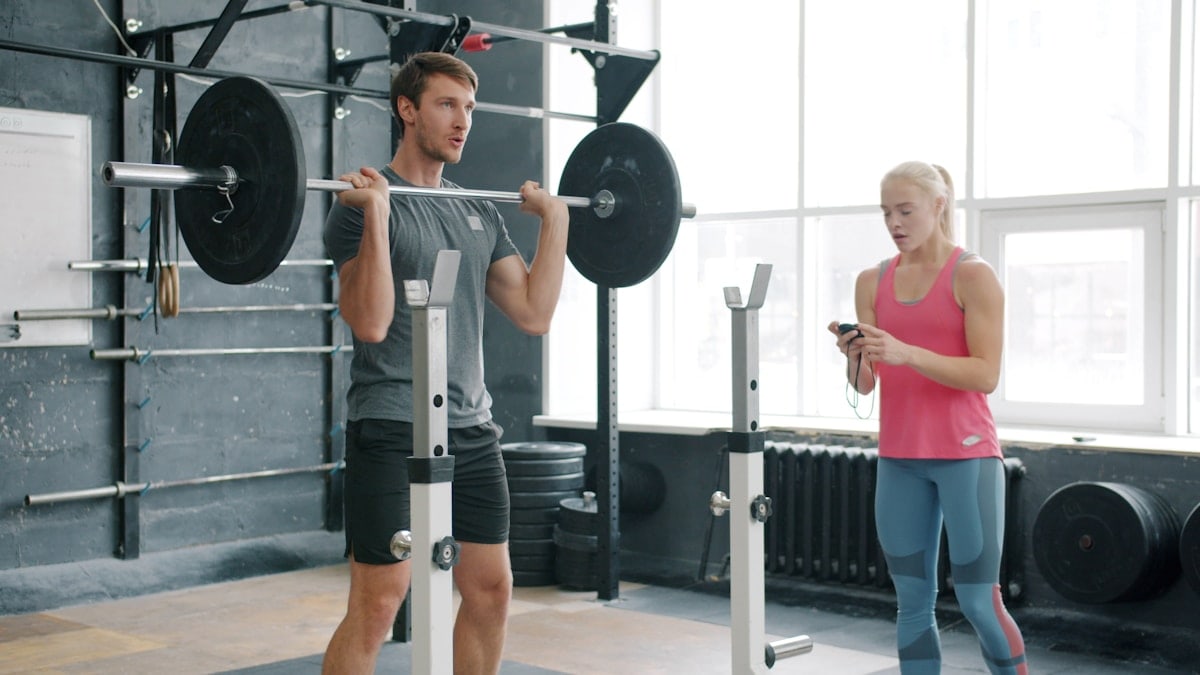 Strong guy is lifting barbell training with weight-lifting indoors in gym working with woman coach. Active lifestyle, motivation and youth concept.